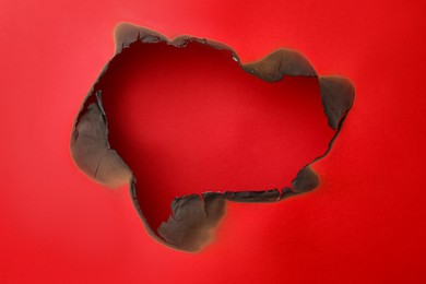 Burnt hole in paper on red background, space for text