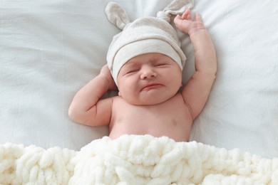 Photo of Adorable little baby with hat sleeping in bed, top view