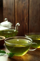 Photo of Fresh green tea in glass cups and leaves on wooden table