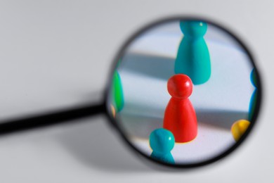 Photo of Magnifying glass over colorful pawns on white background. Recruiter searching employee