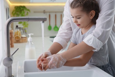 Mother and daughter washing hands with liquid soap together in kitchen, closeup