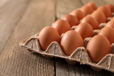 Photo of Fresh raw chicken eggs in carton on wooden table, closeup