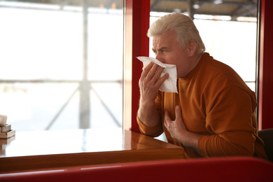 Sick senior man with tissue in cafe. Influenza virus