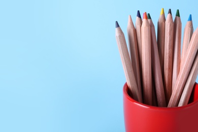 Colorful pencils in cup on light blue background, closeup. Space for text