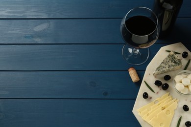 Tasty red wine and different sorts of cheese on blue wooden table, flat lay. Space for text