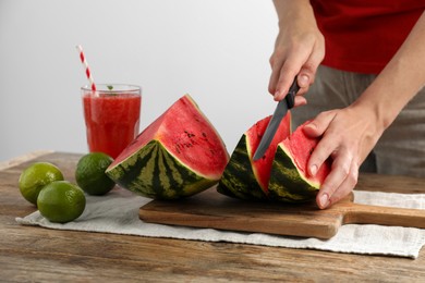 Photo of Woman cutting delicious watermelon at wooden table against light background, closeup