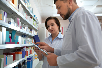 Professional pharmacists near shelves with medicines in modern drugstore