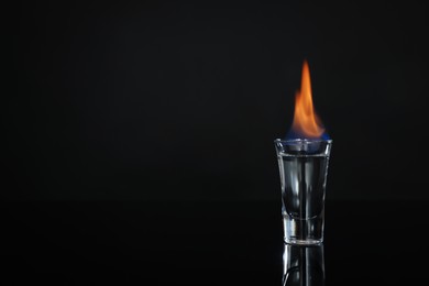 Flaming vodka in shot glass on black background, space for text