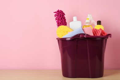 Photo of Bucket with different cleaning supplies on wooden floor near pink wall. Space for text