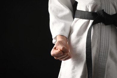 Man wearing keikogi and black belt on dark background, closeup view with space for text. Martial arts uniform