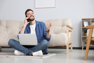 Happy man using smartphone while working with laptop at home, space for text