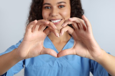 Happy young African-American doctor making heart with hands on light grey background, closeup