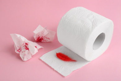 Roll of toilet paper and red feather on pink background. Hemorrhoid problems
