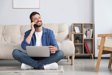 Photo of Happy man talking on smartphone while working with laptop at home