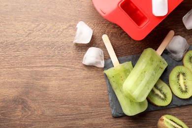 Tasty kiwi ice pops and space for text on wooden table, flat lay. Fruit popsicle