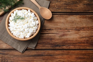Fresh cottage cheese with dill in bowl on wooden table, flat lay. Space for text