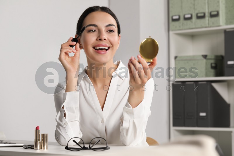 Photo of Young woman using cosmetic pocket mirror while applying makeup indoors