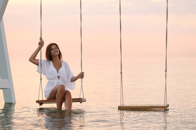 Young woman enjoying sunrise on swing over water