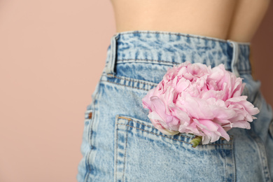 Woman with pink peony bud in pocket on beige background, closeup