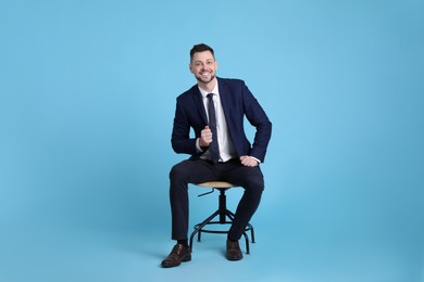 Handsome businessman sitting in office chair on light blue background