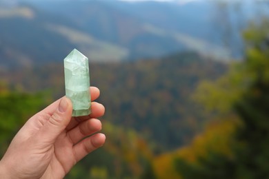 Woman holding crystal in mountains, closeup. Space for text