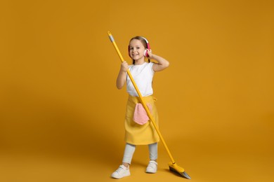 Cute little girl in headphones with broom on orange background
