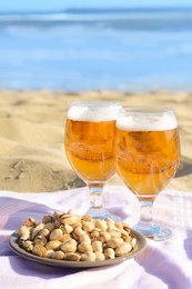 Photo of Glasses of cold beer and pistachios on sandy beach near sea