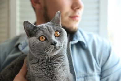 Man with cute cat on blurred background, closeup