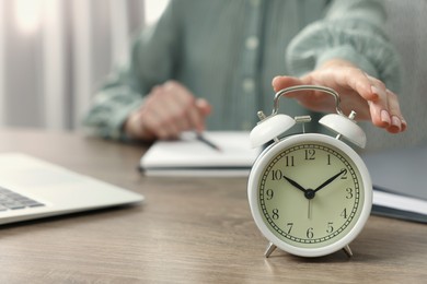 Photo of Woman turning off alarm clock at table, closeup. Space for text