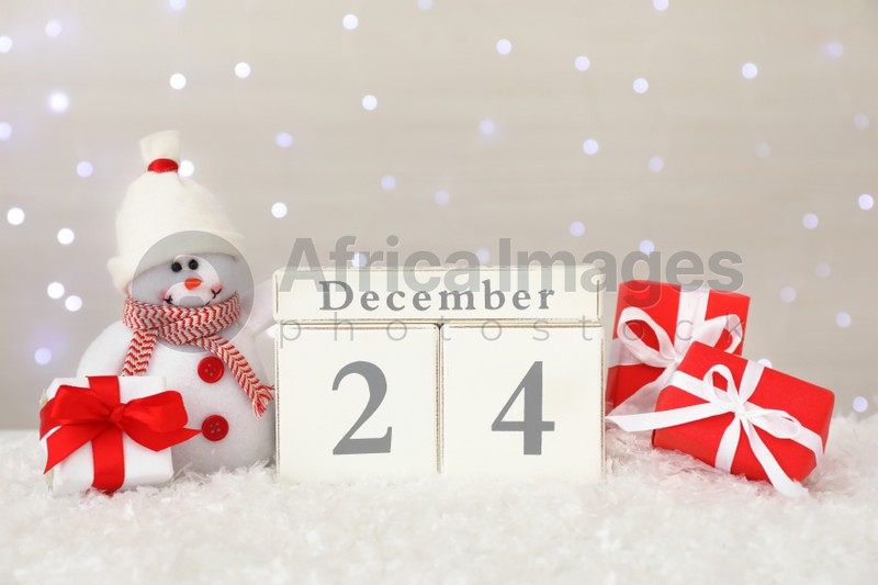 Photo of Christmas Eve - December 24. Wooden block calendar, cute toy snowman and gift boxes on artificial snow