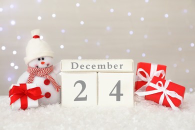 Christmas Eve - December 24. Wooden block calendar, cute toy snowman and gift boxes on artificial snow