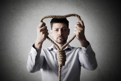 Depressed man with rope noose on light background. Suicide concept