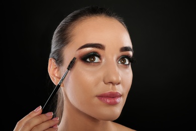 Portrait of young woman with eyelash extensions holding brush on black background