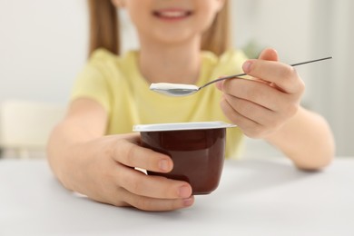 Photo of Cute little girl with tasty yogurt at white table, closeup