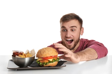 Young hungry man and plate with French fries and tasty burger on white background