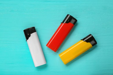 Photo of Stylish small pocket lighters on turquoise wooden background, flat lay