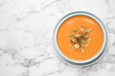 Tasty creamy pumpkin soup with croutons, seeds and dill in bowl on white marble table, top view. Space for text