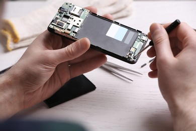 Technician fixing mobile phone at table, closeup. Device repair service