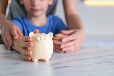 Mother and son with piggy bank at marble table indoors, closeup