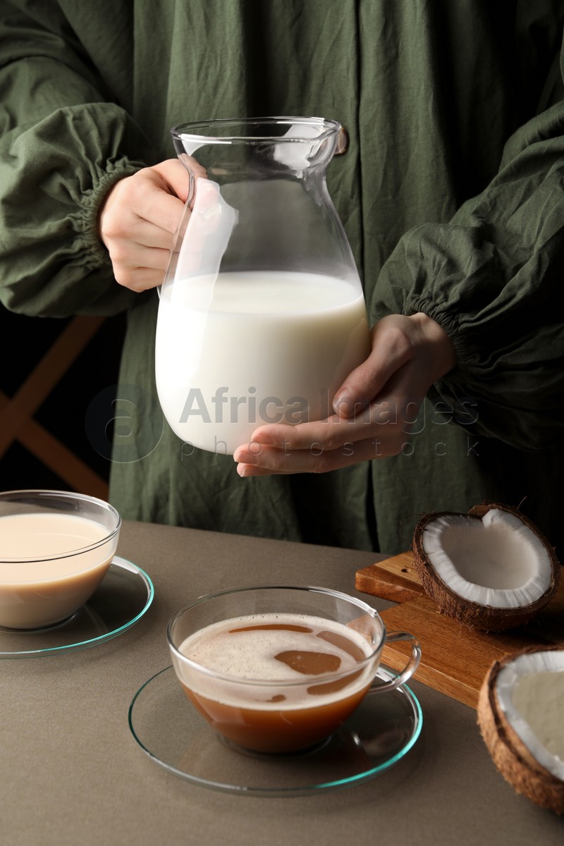 Photo of Woman with jug of tasty coconut milk at table, closeup