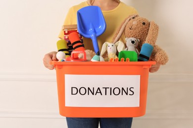 Woman holding donation box with toys against light background, closeup