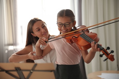 Young woman teaching little girl to play violin indoors