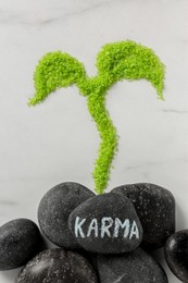 Photo of Stone with word Karma and sprout made of light green sea salt on white marble table, flat lay