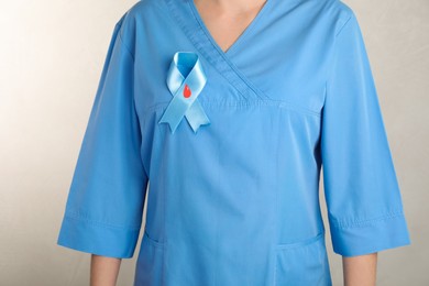 Photo of Doctor with light blue ribbon and paper blood drop, closeup. World Diabetes Day
