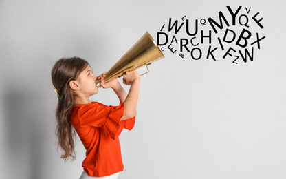 Adorable little girl with vintage megaphone and letters on light background. Speech therapy concept