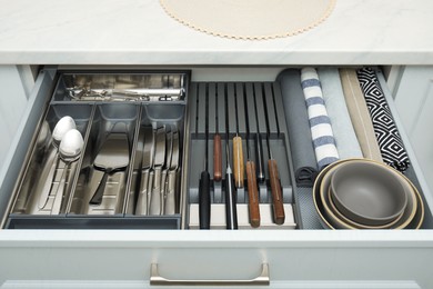 Photo of Open drawer of kitchen cabinet with different utensils, dishware and towels