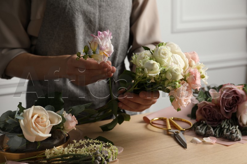 Photo of Florist creating beautiful bouquet at wooden table indoors, closeup