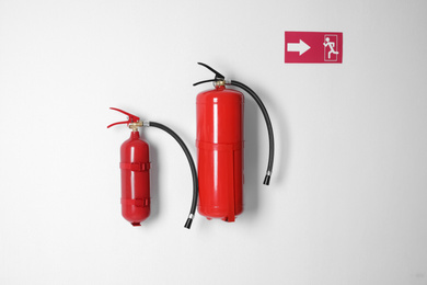 Different fire extinguishers and emergency exit sign on white wall