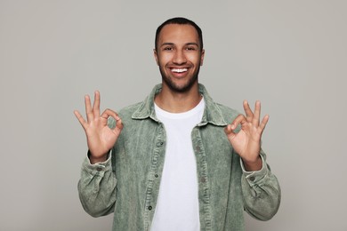 Photo of Smiling African American man showing ok gesture on light grey background