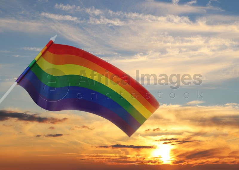 Bright rainbow LGBT flag against sky at sunset